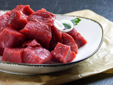 Rinder Gulasch vom Bugstück vom EIFEL Rind angerichtet mit Zwiebelringen in einer Schüssel auf Backpapier mit Schieferhintergrund