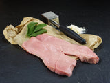 Kalb Oberschalenschnitzel präsentiert auf Backpapier mit einem Fleischklopfer und Minze auf schwarzer Schieferplatte