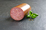 Land Cervelatwurst am Stück angerichtet mit Pfeffer Senfkörnen und Basilikum auf Schieferhintergrund