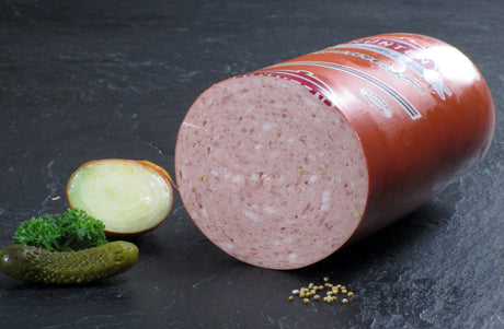 Eine halbe Bierwurst vom EIFEL Schwein angerichtet mit einer halben Zwiebel Petersilie Senfkörnern und einer Gewürzgurke auf Schieferhintergrund