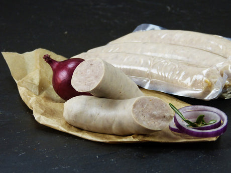 Drei grobe gebrühte Bratwürste verpackt und eine halbierte Bratwurst angerichtet mit einer roten Zwiebel und zwei roten Zwiebelringen  mit Thymian auf Backpapier mit Schieferhintergrund