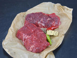 Zwei Argentinisches Rumpsteak angerichtet mit Kräuterbutter einer grünen Chilischote und einer roten auf Backpapier mit Schieferhintergrund