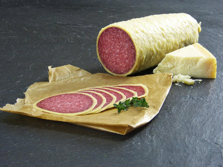 Salami im Käsemantel geschnitten auf Backpapier mit Parmesankäse und Kräutern auf Schieferhintergrund