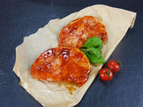 Zwei Schweinerückensteaks Barbecue angerichtet mit Basilikum und Tomaten auf Backpapier mit Schieferhintergrund