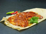 Zwei Schweinenackensteaks Barbecue angerichtet mit einer roten und einer Grünen Chilischote und Basilikum auf Backpapier mit Schieferhintergrund