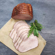 Kesselschinken vom EIFEL Schwein am Stück und 7 Scheiben aufgeschnitten mit verschiedenen Kräutern auf Holzpapier und Schieferhintergrund