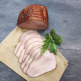 Kesselschinken vom EIFEL Schwein am Stück und 7 Scheiben aufgeschnitten mit verschiedenen Kräutern auf Holzpapier und Schieferhintergrund