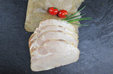 Schweinegrillbraten Aufschnitt angerichtet auf Backpapier mit Tomaten und Schnittlauch auf Schieferhintergrund