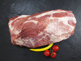Schweinekamm ohne Knochen am Stück mit gelber Peperonie und Tomaten auf Schieferhintergrund von oben fotografiert