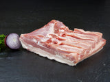 Schweinebauch ohne Rippe mit roter Zwiebel und Petersilie auf Schieferhintergrund
