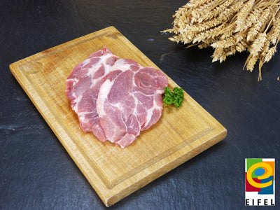 Kammsteak vom EIFEL Schwein auf Holzbrett mit Ähren auf Schieferhintergrund