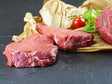 Argentinische Rindersteakhüfte portioniert mit Tomaten und Salat auf Schieferhintergrund
