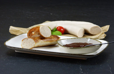 Bratwurst vom EIFEL Schwein mit einer Schüssel Gewürzketchup Basilikum und einer Cherrytomate auf Schieferhintergrund