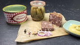 Hausmacher Blutwurst angerichtet auf Backpapier mit groben Salz und Pfferkörnern roten Zwiebelscheiben und einem kleinen Glas eingelegte Gurken sowie einer kleinen Schale Senf