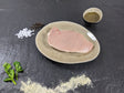 Schweinerückensteak Pfeffer und Salz auf Teller angerichtet mit einer Schale Marinade, groben Salz und Pfefferkörnern und Kräutern auf Schieferhintergrund