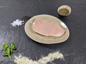 Schweinerückensteak Pfeffer und Salz auf Teller angerichtet mit einer Schale Marinade, groben Salz und Pfefferkörnern und Kräutern auf Schieferhintergrund