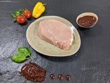Schweinerückensteak Barbecue auf Teller angerichtet mit einer Schale Barbecue Marinade Tomaten Paprika und Kräutern auf Schieferhintergrund