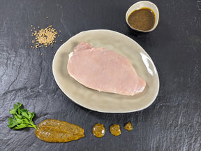 Schweinerückensteak Senfzauber auf Teller angerichtet mit einer Schale Senf Marinade Senfkörnern und Kräutern auf Schieferhintergrund