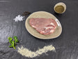 Schweinenackensteak Pfeffer und Salz auf Teller angerichtet mit einer Schale Marinade groben Salz und Pfefferkörnern und Kräutern auf Schieferhintergrund