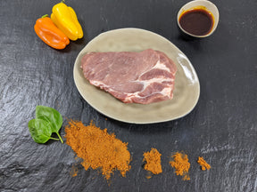Schweinenackensteak Paprika auf Teller angerichtet mit einer Schale Marinade Paprikas Kräutern und Gewürzen auf Schieferhintergrund