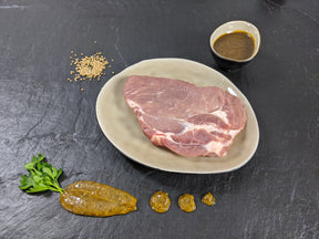 Schweinenackensteak Senfzauber auf Teller mit einer Schale Marinade Senfkörnern und Kräutern auf Schieferhintergrund