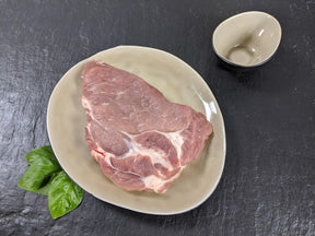 Schweinenackensteak natur auf Teller mit Kräutern auf Schieferhintergrund