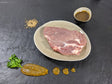 Schweinebauchscheibe Senfzauber auf Teller angerichtet mit einer Schale Marinade Senfkörnern und Kräutern auf Schieferhintergrund