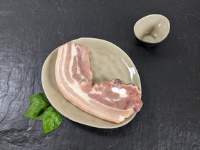 Schweinebauchscheibe natur auf Teller angerichtet mit Kräutern auf Schieferhintergrund