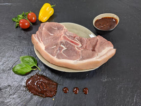 Holzfällersteak Barbecue auf Teller angerichtet mit einer Schale Marinade Tomaten und Kräutern auf Schieferhintergrund