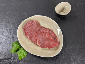 Rumpsteak natur auf Teller angerichtet mit Kräuter auf Schieferhintergrund