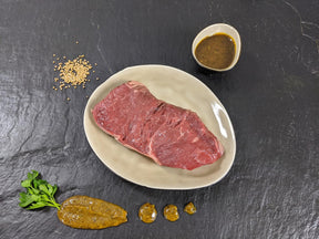 Rumpsteak Senfzauber auf Teller angerichtet mit einer Schale Marinade Senfkörnern und Kräutern auf Schieferhintergrund