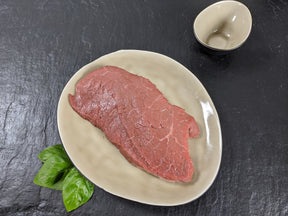 Rinderhüftsteak natur auf Teller angerichtet mit Kräutern auf Schieferhintergrund