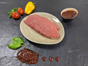 Rinderhüftsteak Barbecue auf Teller angerichtet mit einer Schale Marinade Tomaten Paprika und Kräutern auf Schieferhintergrund