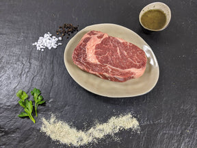 Entrecôte Pfeffer und Salz auf Teller mit einer Schale Marinade groben Salz und Pfefferkörnern und Kräutern auf Schieferhintergrund