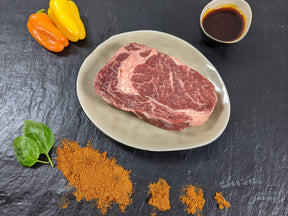Entrecôte Paprika auf Teller angerichtet mit einer Schale Marinade Paprika Kräutern und Paprikapulver auf Schieferhintergrund