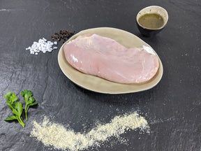 Putensteak Pfeffer und Salz auf Teller angerichtet mit einer Schale Marinade groben Salz und Pfefferkörnern und Kräutern auf Schieferhintergrund
