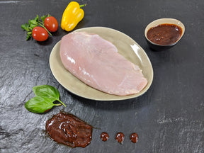 Putensteak Barbecue auf Teller angerichtet mit einer Schale Barbecue Soße Tomaten Kräutern und Paprika auf Schieferhintergrund