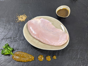 Putensteak Senfzauber auf Teller angerichtet mit einer Schale Marinade Senfkörnern und Kräutern auf Schieferhintergrund