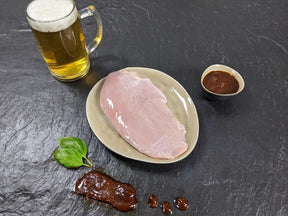 Putensteak Braumeister auf Teller angerichtet mit einer Schale Braumeister Marinade einem Glas Bier und Kräutern auf Schieferhintergrund