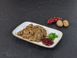 Hirschgulasch in Preiselbeer Rotweinsauce auf Teller angerichtet mit Preiselbeeren Petersilie und Nüssen auf Schieferhintergrund