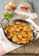 Bratkartoffeln gegart auf Holzbrett  mit Serviertte und Speck Basilikum und Zwiebeln im Hintergrund