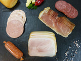 Auswahl aus Bauernschinken und Metzgerschinken vom EIFEL Schwein Brühwurstaufschnitt gemischt Pfeffersalami und Zwiebelmettwurst angerichtet auf Schieferhintergrund mit Käsewürfeln, Chilischoten und einem Brötchen