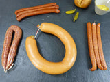 Wanderpaket mit Fleischwurst Rohessern luftgetrockneter Mettwurst mit Senf Brötchen und Gewürzgurken dekoriert auf Schieferhintergrund