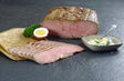 Roastbeefbraten geschnitten angerichtet auf Backpapier mit gekochtem Ei, Petersilie und Remoulade in einer kleinen Schüssel auf Schieferhintergrund