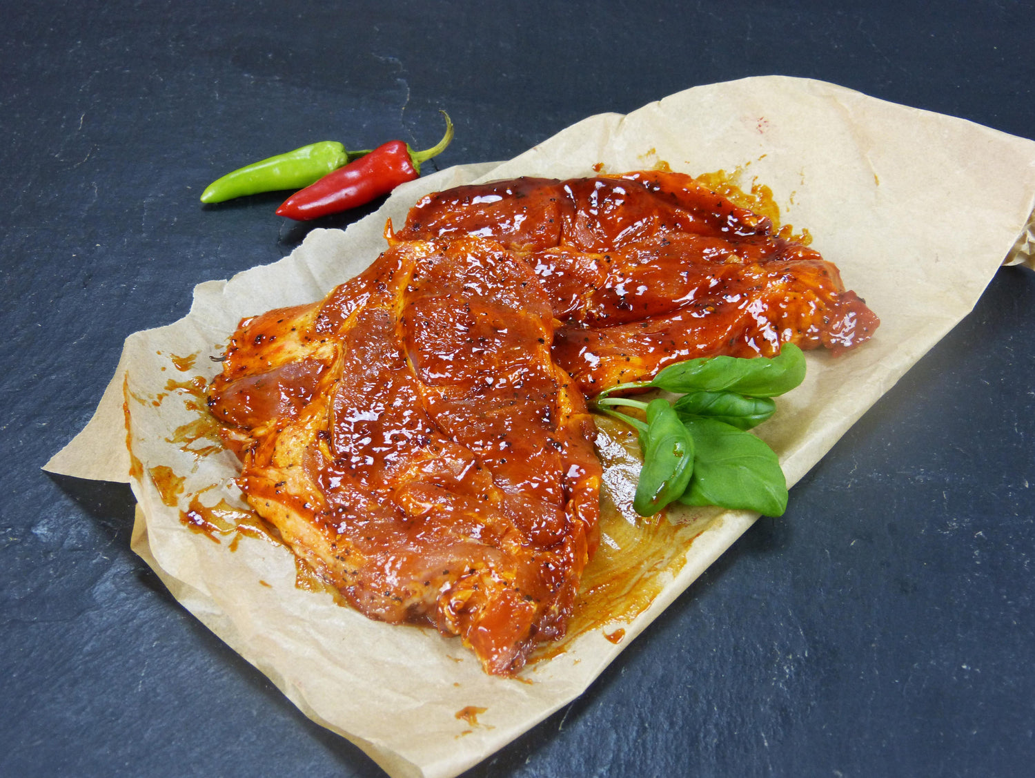 Schweinenackensteak Barbecue mit Basilikum und Peperoni auf Schieferhintergrund