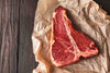 T Bone Steak von der Färse auf Backpapier angerichtet auf Holzhintergrund